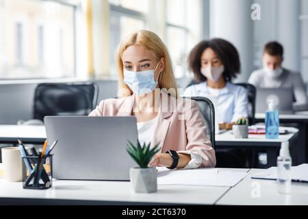 New normal and modern job in office. European and african american managers work on laptops in workplaces with antiseptic during epidemic Stock Photo