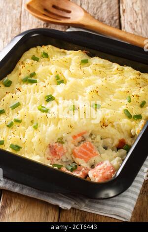 Traditional english fish pie with mashed potatoes and salmon close-up in a baking dish on the table. vertical
