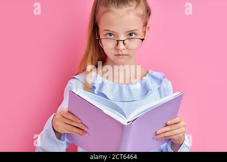 adorable caucasian girl in eyeglasses read a book isolated, smart intelligent child love learning, studying, keen on education Stock Photo