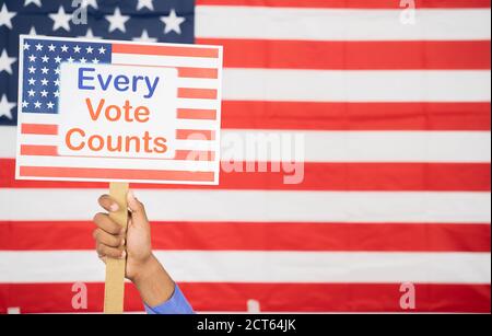 Hands Holding Every Vote counts sign board with US Flag as Background with copy space - Concept of voter rights and US election. Stock Photo