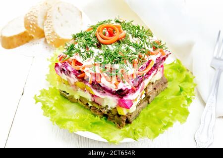 Puff salad with beef, boiled potatoes, pears, spicy Korean carrots, seasoned with mayonnaise and garnished with dill on green lettuce in plate, bread Stock Photo