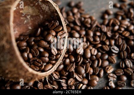 Roasted arabica coffee beans scattered on a wooden table from a coconut. Fresh coffee beans.