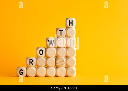 The word growth on stacked wooden cubes against yellow background. Financial or business growth concept. Stock Photo