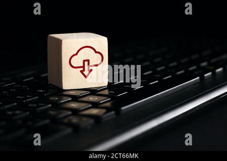 Cloud computing download icon on wooden cube with computer keyboard against black background. Remote download technology concept. Stock Photo