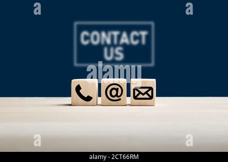 Phone and e-mail icons on wooden cubes with contact us text on blue background. Website page contact us or e-mail marketing concept. Stock Photo
