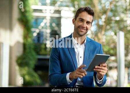 Smiling young businessman using a digital tablet while standing outside Stock Photo