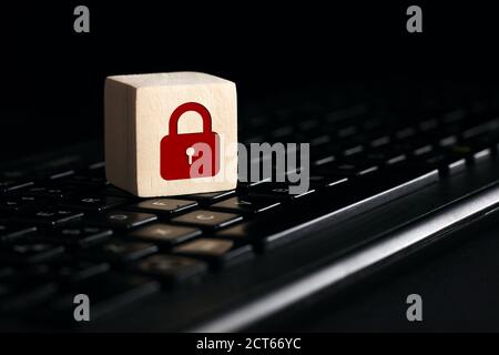 Padlock symbol on wooden cube with computer keyboard against black background. Data protection or cyber security concept. Stock Photo