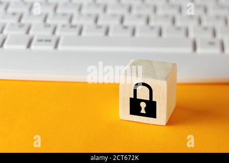 Padlock symbol on wooden cube with computer keyboard background. Data protection or cyber security concept. Stock Photo
