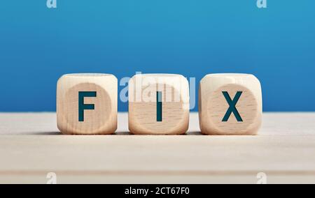 The word fix on wooden cubes against blue background. Fixing, repairing or solution concept. Stock Photo
