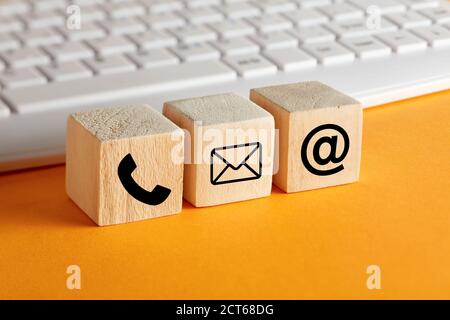 Online business communication symbols of telephone, email and mail address on wooden cubes with computer keyboard background. Contact us or e-mail mar Stock Photo