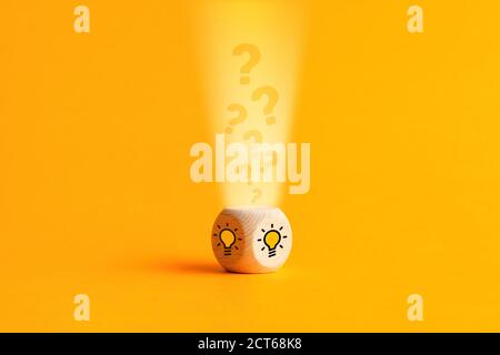 Question mark icons are filling into a wooden cube with light bulb icons. Idea generation, decision making or problem solving in business or education Stock Photo