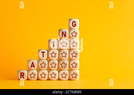 The word rating with increasing performance stars on wooden cubes against yellow background. Improvement in service rating and customer evaluation con Stock Photo