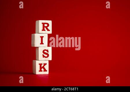 The word risk on wooden cubes against red background. Risk and uncertainty in business and decision making strategy concept. Stock Photo