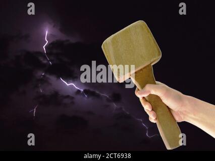 Hand holding big wooden hammer on thunderbolt in night background Stock Photo
