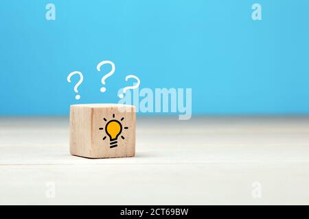 Creative idea, solution or problem solving concept. Question mark and light bulb icons on wooden cube against blue background. Stock Photo