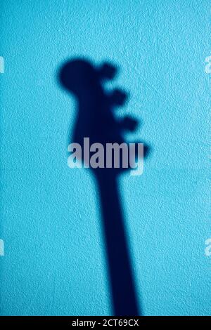Silhouette or shadow of an electric bass guitar on a blue textured wall with copy space. Stock Photo