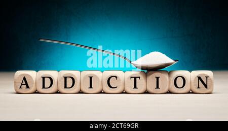 Sugar addiction, diabetes and healthy nutrition concept. The word addiction on wooden cubes with a spoon full of granulated sugar. Stock Photo