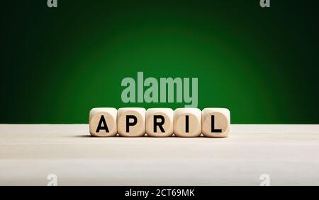 The month April written on wooden cubes with green spring background with copy space. Month of the year. Stock Photo
