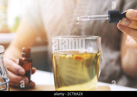 dietary supplements and vitamins - woman adding drops in cup of tea with dropper. Stock Photo