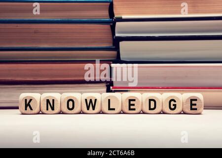 The word knowledge on wooden cubes against stacked books background. Education, wisdom and learning concept. Stock Photo