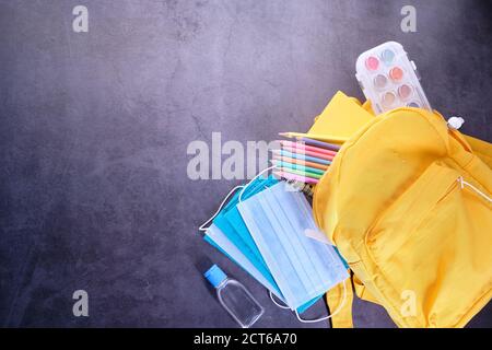 yellow backpack, stationery, mask and sanitizer on black background  Stock Photo