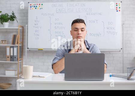 Communicate with students online remotely and video call with teacher. Concentrated man looking at laptop and listening to students answer Stock Photo