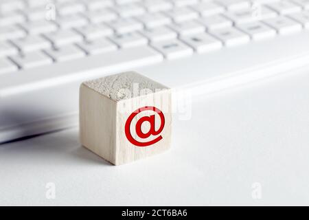 Wooden block with email at symbol with computer keyboard background on white. Customer care, support or e-mail connection concept. Stock Photo