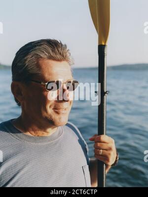 Portrait of middle aged man holding sea kayak paddle at dusk Stock Photo