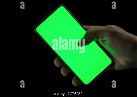 Isolated human hand holding a green screen smartphone on black background,hi tech addiction concept Stock Photo