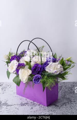 Festive bouquet of white eustoma and blue lisianthuses with delicate greenery lying in a purple cardboard bag. Stock Photo