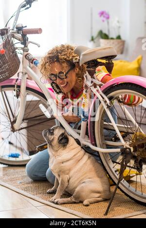 Best friend forever little adorable pug dog at home with her female cheerful owner repairing a coloured happy bike - concept of people and animal frie Stock Photo