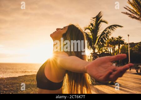 Athlete sporty and beautiful young woman stretch and breathe after workout in outdoor with sunset and sunlight in background with ocean and sky - heal Stock Photo