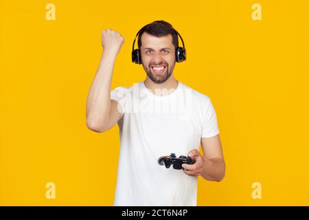 Young man with beard in white t-shirt gamer playing video games with headphones annoyed and frustrated screaming with anger, crazy and screaming with raised hand, anger concept. Stock Photo