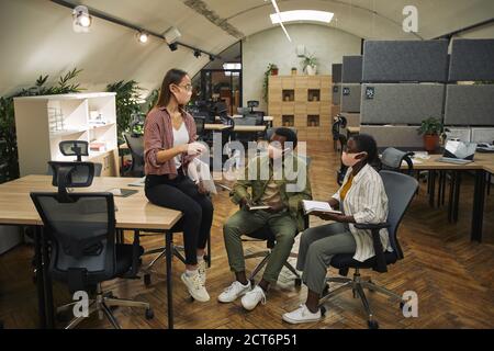 Full length portrait of three contemporary business people wearing masks while discussing work project in modern office post pandemic Stock Photo