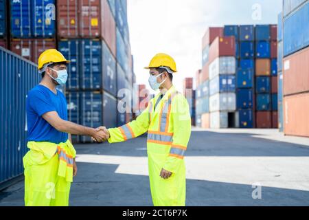 Workers wearing protective mask to Protect Against Covid-19 discussion shaking hands in shipping yard at container cargo. Stock Photo