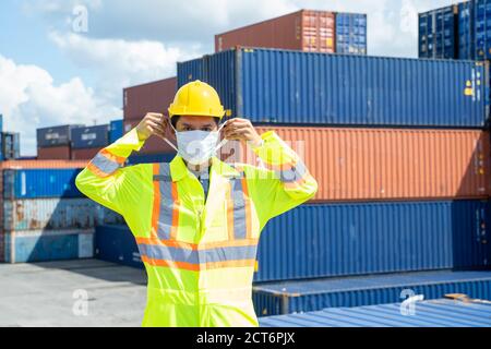 Container worker wearing protection face mask during corona virus and flu outbreak and yellow safety hard hat helmet standing at container yard,Import Stock Photo