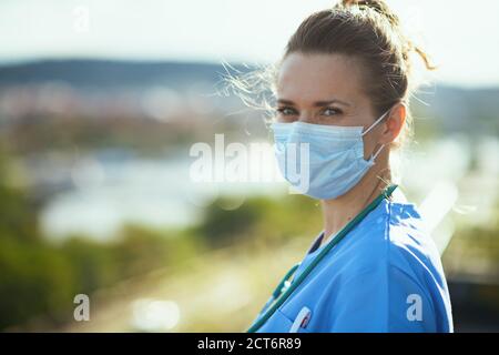 covid-19 pandemic. Portrait of modern physician woman in uniform with medical mask outside on the city street. Stock Photo
