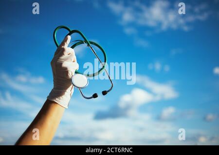 covid-19 pandemic. Closeup on medical practitioner woman with stethoscope and rubber gloves outdoors in the city against sky. Stock Photo