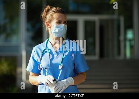 coronavirus pandemic. modern physician woman in uniform with stethoscope, medical mask and cup of coffee looking into the distance outdoors near clini Stock Photo