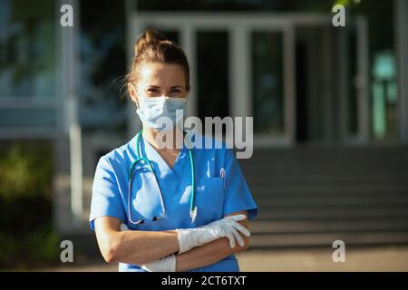 covid-19 pandemic. Portrait of confident modern medical doctor woman in uniform with stethoscope and medical mask outside near hospital. Stock Photo