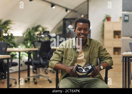 Portrait of young African-America man holding VR gear and smiling at camera sitting in modern office, copy space Stock Photo