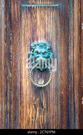 Detail of an ancient wooden door aged by time with a metal lion head shaped door knocker with a ring in the mouth Stock Photo