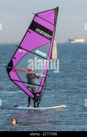 Southend on Sea, Essex, UK. 21st Sep, 2020. The weather dawned foggy and cloudy in Southend on Sea but broke into a warm and sunny afternoon. People are out enjoying the afternoon high tide with some taking to the water. A female windsurfer is sailing past a swimmer Stock Photo