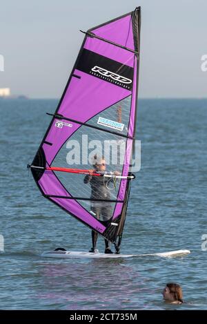 Southend on Sea, Essex, UK. 21st Sep, 2020. The weather dawned foggy and cloudy in Southend on Sea but broke into a warm and sunny afternoon. People are out enjoying the afternoon high tide with some taking to the water. A female windsurfer is sailing past a swimmer Stock Photo