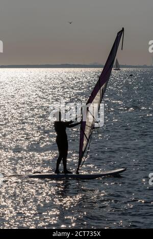 Southend on Sea, Essex, UK. 21st Sep, 2020. The weather dawned foggy and cloudy in Southend on Sea but broke into a warm and sunny afternoon. People are out enjoying the afternoon high tide with some taking to the water. A female windsurfer on the calm waters, silhouette by glistening sea Stock Photo