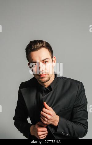 Young handsome man in a black suit, looking at the camera, against plain studio background Stock Photo