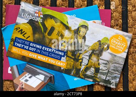 unsolicited mail junk mail on doormat - RNLI Lifeboats the RNLI charity that saves lives at sea - they're giving everything they've got in this crisis Stock Photo
