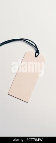 The price tag made of cardboard is empty without inscriptions on a light background. Light falls from one side, there is a shadow. Stock Photo
