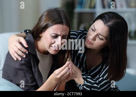 Sad wife after divorce being comforted by a friend on a couch in the living room at home Stock Photo