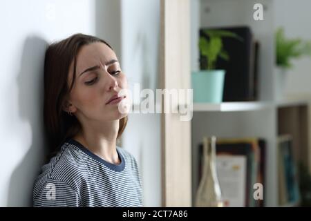 Depressed woman complaining alone leaning on a wall at home Stock Photo